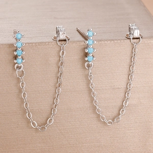 Detail of silver chain earrings with four round blue turquoise stones on a champagne base