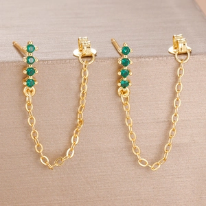 Macro detail of gold chain earrings featuring four claw-set green zircon gemstones