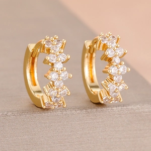 Close-up of gold-plated huggie earrings with sparkling clear zircon inlay on beige stand
