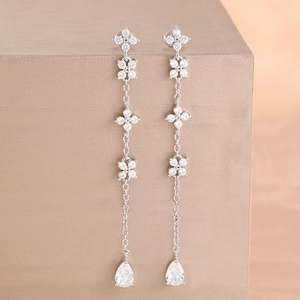 Detail of silver drop earrings featuring zircon clover charms and teardrop pendants