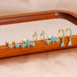 Détail de boucles d'oreilles fleurs dorées avec pierres turquoise sur soie champagne