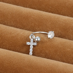 Détail macro d'un piercing de nombril argenté avec zircons et pendentif en forme de croix