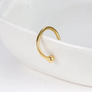 Clip d'oreille et anneau de nez dorés en forme de C avec boule sur un bol en céramique