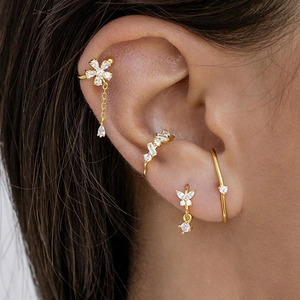 Détail de manchettes d'oreilles dorées avec strass et breloques fleur et papillon