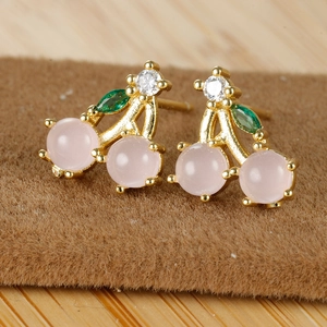 Macro detail of 18K gold cherry earrings with pink crystal and green gems