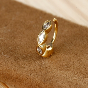 Gedetailleerde close-up van gouden oorring met marquise zirkoon op bruine achtergrond