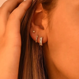 Detailed close-up of a three-piece gold earring set with cubic zirconia on a female model