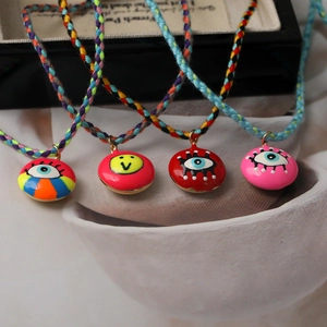 Close-up of colorful woven cords with enamel evil eye and smiley face pendants on silk