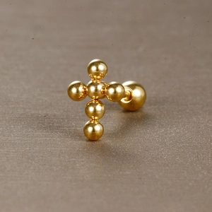 Gros plan d'un piercing croix en acier inoxydable doré avec fermoir à bille vissée