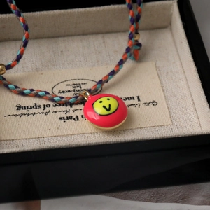 Detailed macro view of a colorful braided rope bracelet with a red enamel smiley face charm