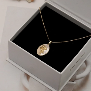 Détail du collier fleur de nacre dorée dans une boîte cadeau blanche haut de gamme