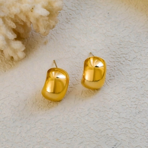 Polished 18K gold bean earrings on minimalist textured stone and white coral background