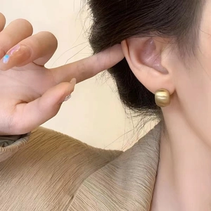 Matte gold bean-shaped stud earrings featuring a brushed metal texture on a model