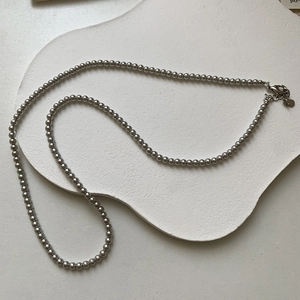 Détail d'un collier de perles grises avec lustre métallique et pendentif cœur