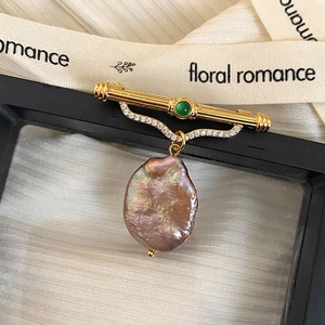 Detailed close-up of a vintage brooch with green gemstone and baroque purple pearl