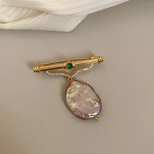 Detail of baroque pearl brooch with green gemstone and gold finish on elegant neutral surface
