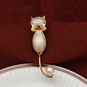 Détail d'une broche chat dorée sertie de zircons avec nœud rubis et perle rose élégante