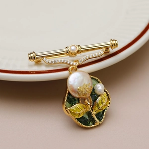 Detail of vintage gold brooch with baroque pearl and green enamel floral pattern