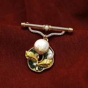 Macro detail of a baroque pearl brooch with enamel leaves on dark red fabric background