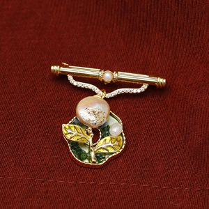Detailed close-up of Baroque pearl brooch with enamel leaves on red fabric