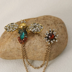 Close-up of vintage bee brooch with green emerald, ruby stones and gold link chains
