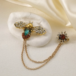 Vintage bee brooch with green emerald and gold chains on elegant silk background