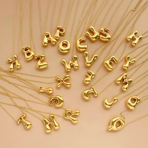 Colliers lettres ballons en or 18 carats A-Z disposés en rayon sur fond beige
