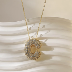 Macro-opname van gouden ketting met met kristal bedekte letter C-hanger op golfachtergrond