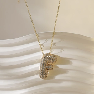 Macro-opname van gouden letter F hanger met pavé-kristallen aan een fijne ketting