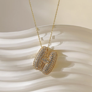 Detailopname van de gouden letter H hanger met glanzende zirkonia aan een fijne ketting
