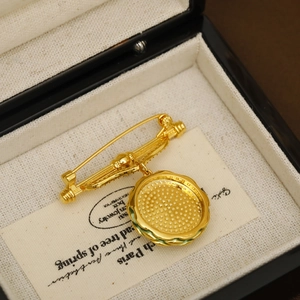 Vintage style gold-plated brooch with textured circular pendant on a black jewelry box
