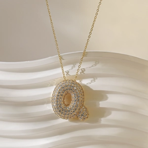 Macro-opname van gouden letter Q-hanger met witte zirkonia's aan een fijne ketting