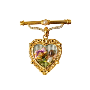 Détail d'une broche vintage en forme de cœur avec fleurs roses et perles sur blanc