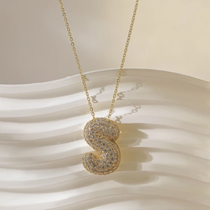 Macro-detail van gouden letter S hanger met zirkoon op witte keramische presentatiestandaard