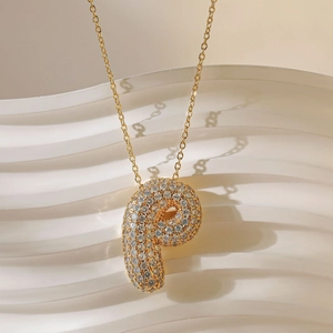 Macro-opname van gouden letter P hanger met kristallen op een elegant wit golvend vlak