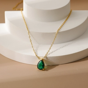 Detail of 18k gold chain with pear-cut green zircon pendant on white display stand