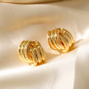 Macro view of gold 18K plated geometric spiral hoop earrings on champagne silk fabric
