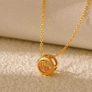Macro view of gold zodiac necklace with pink gemstone and hollowed-out constellation symbols