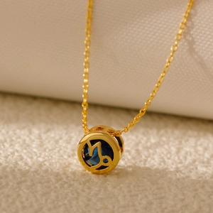 Close-up of gold Capricorn pendant with dark blue stone and hollowed zodiac pattern
