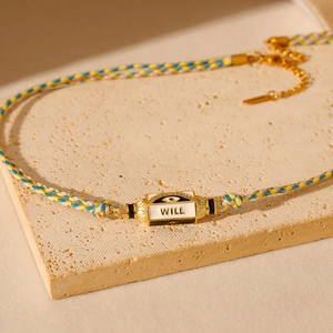 Vue macro d'un bracelet tressé coloré avec charm Evil Eye doré et gravure 'WILL'