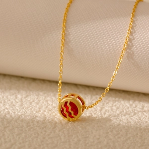 Macro shot of gold hollow Aquarius necklace with a ruby red zircon stone and wave symbol