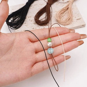 Hand holding 1mm waxed polyester cord through various beads for DIY jewelry making