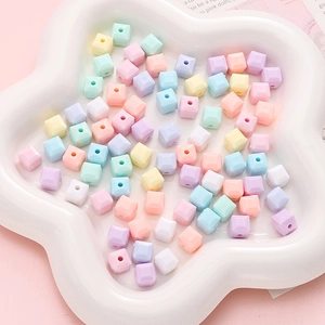 Dettaglio di perline a cubo in acrilico macaron da 8mm sparse su un vassoio bianco