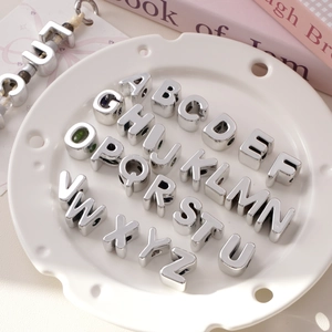 Set of 26 silver acrylic alphabet beads for DIY jewelry making in a white ceramic dish