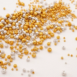 Golden and silver glass seed beads for DIY jewelry making on white leather background