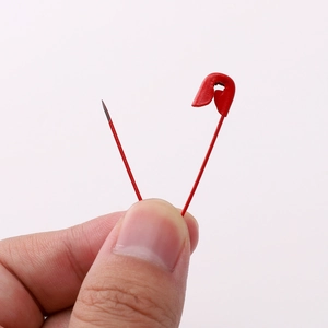 Single red painted iron safety pin held by hand showcasing compact size and metal finish