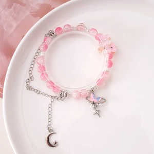 Handmade pink beaded bracelet with butterfly and crescent moon charms on a white plate