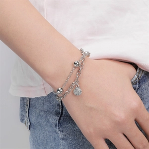Detalle de pulsera de doble cadena plateada con cuentas metálicas y un colgante de concha
