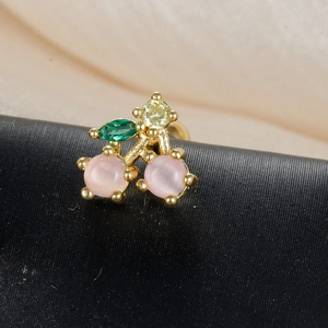Macro shot of cherry-shaped gold earring with pink opal stones and green zircon leaf