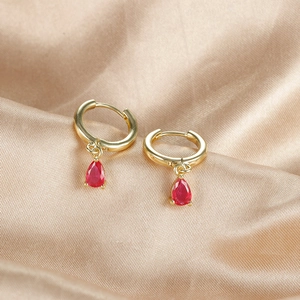 Elegant gold hoop earrings with pear-shaped red zircon drops on champagne silk fabric